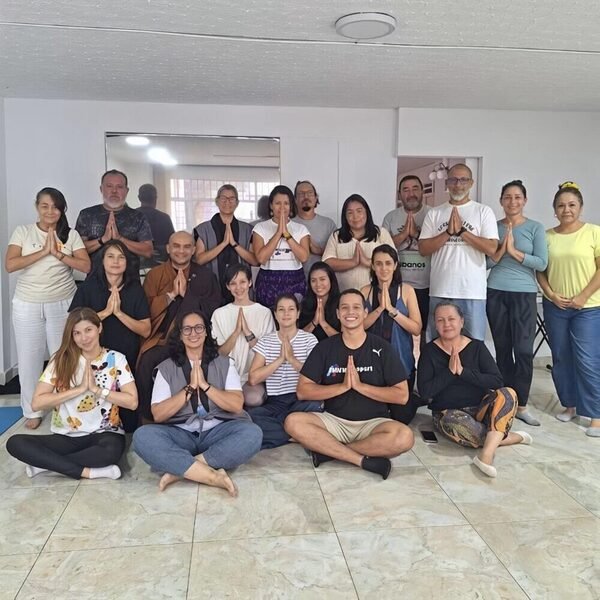 Grupo de practicantes de pie y sentados en un salón, con las manos juntas en gesto de meditación, junto a un monje.