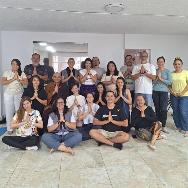 Grupo de practicantes de pie y sentados en un salón, con las manos juntas en gesto de meditación, junto a un monje.