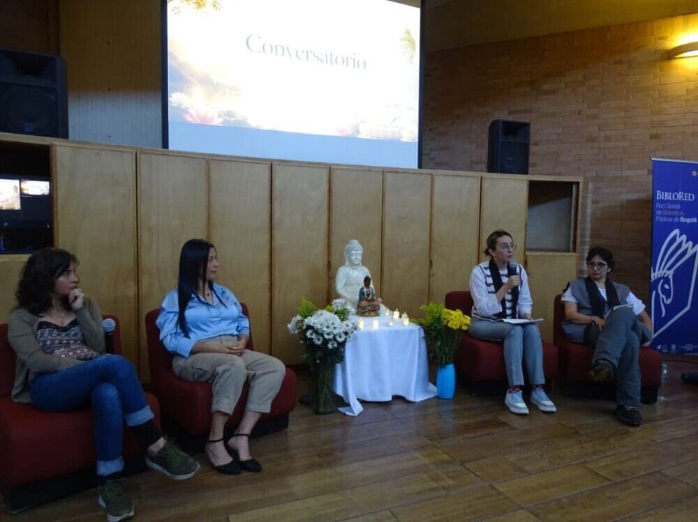 Panel de mujeres en un conversatorio en BibloRed, con altar central con figuras de Buda y flores.