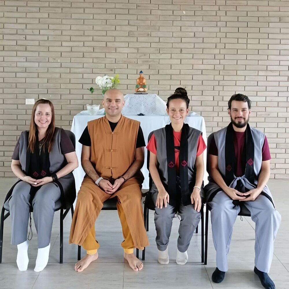 Cuatro personas sentadas en fila frente a un altar con figura de Buda, en un salón de paredes de ladrillo.