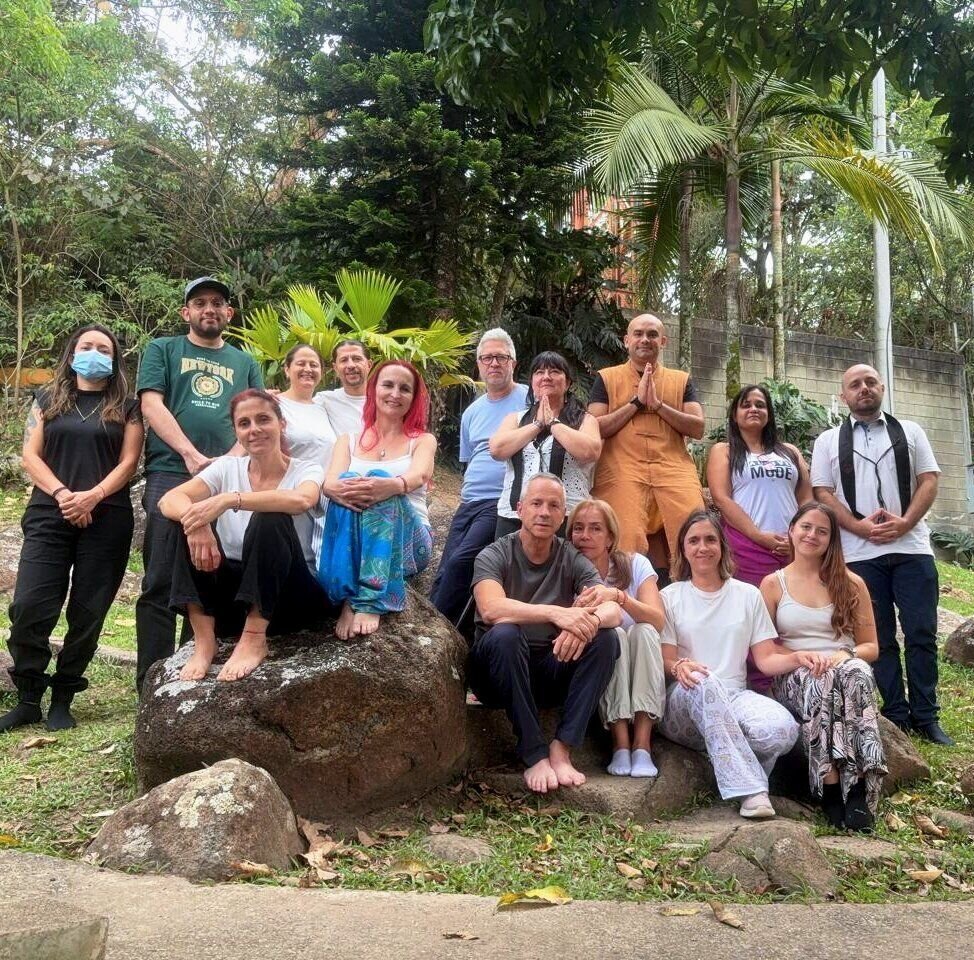 Grupo de practicantes posando sobre rocas en un jardín tropical, con un monje con túnica naranja en el centro.