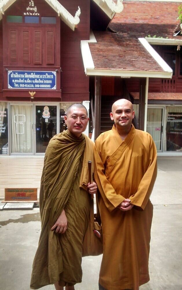 Dos monjes budistas posan frente a un templo tradicional tailandés.