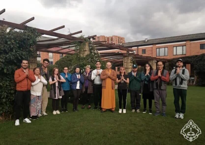 Grupo de practicantes de pie en un jardín, con las manos juntas en gesto de meditación.