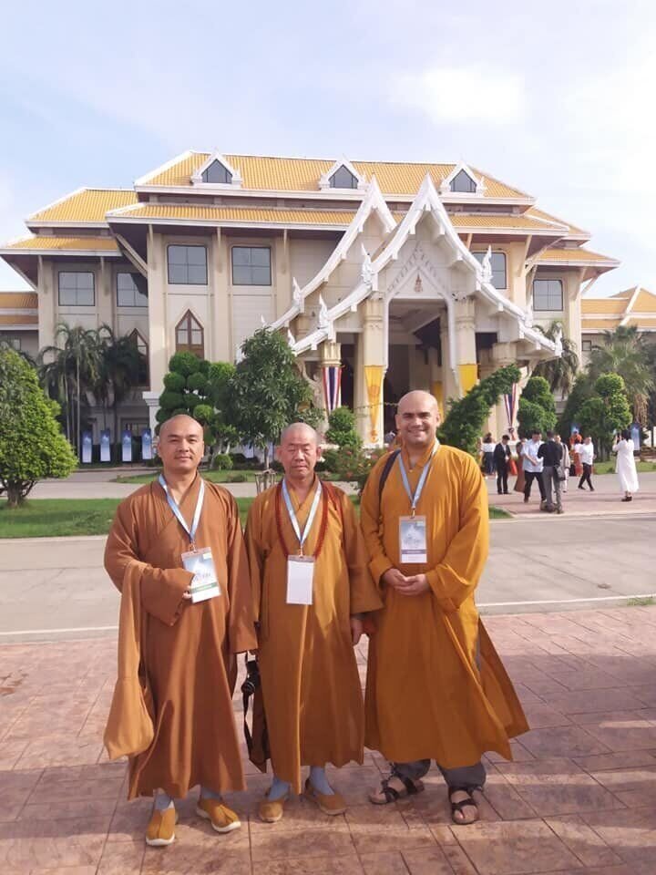 Tres monjes budistas de pie frente a un palacio o templo tailandés.