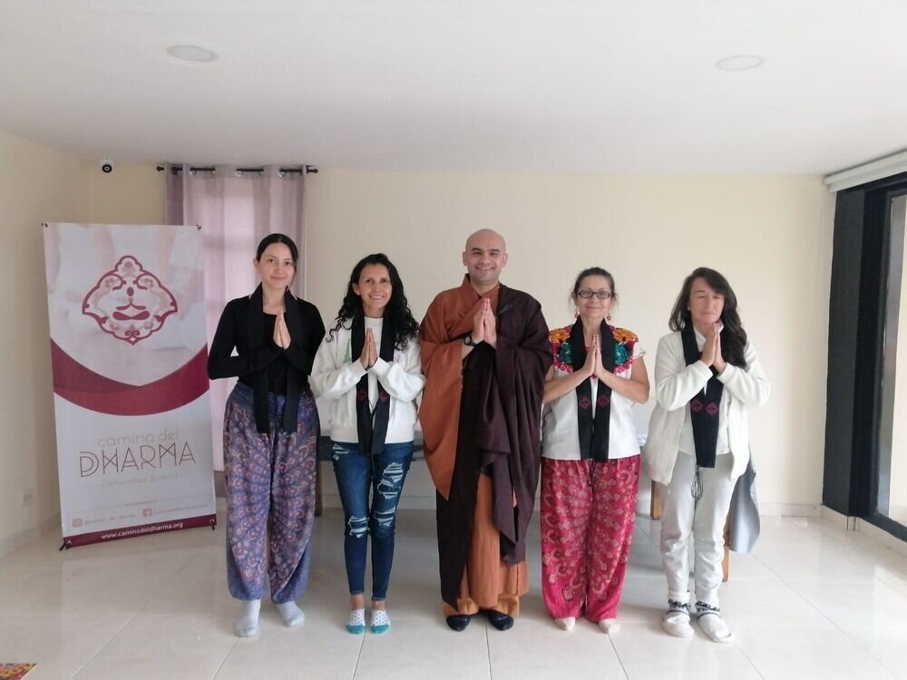 Cinco personas de pie con las manos juntas en gesto de meditación junto a un monje, frente a un pendón de Camino del Dharma.