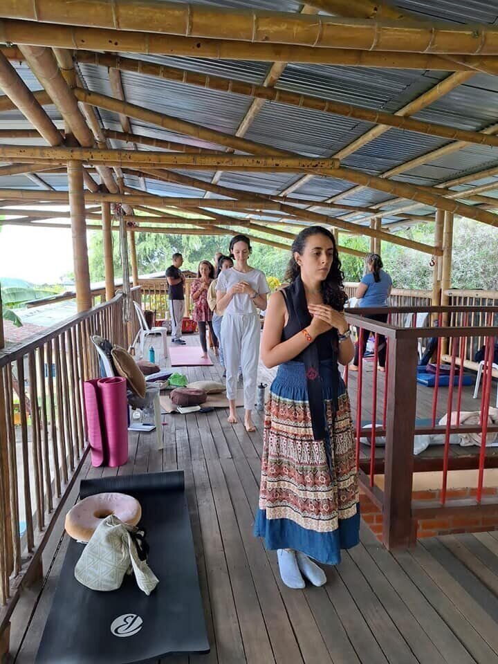Grupo de personas de pie con las manos juntas en el pecho, caminando en fila sobre una terraza de bambú.