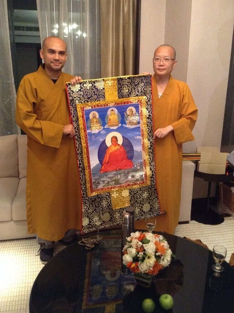 Dos monjes sostienen juntos un thangka con la imagen de Amitābha rodeado de otros budas.