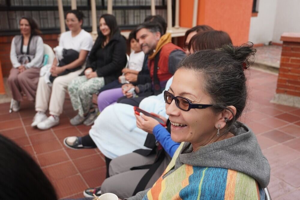 Grupo de personas sentadas conversando y sonriendo en un patio con paredes de color naranja.